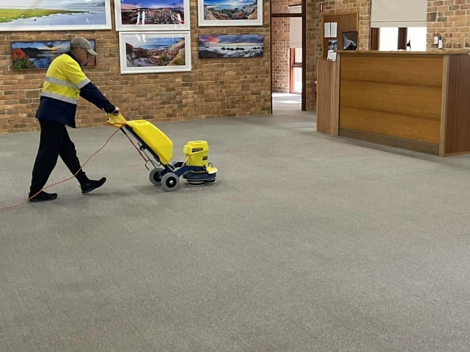 Technician using a rotary machine to clean commercial carpet in a reception area
